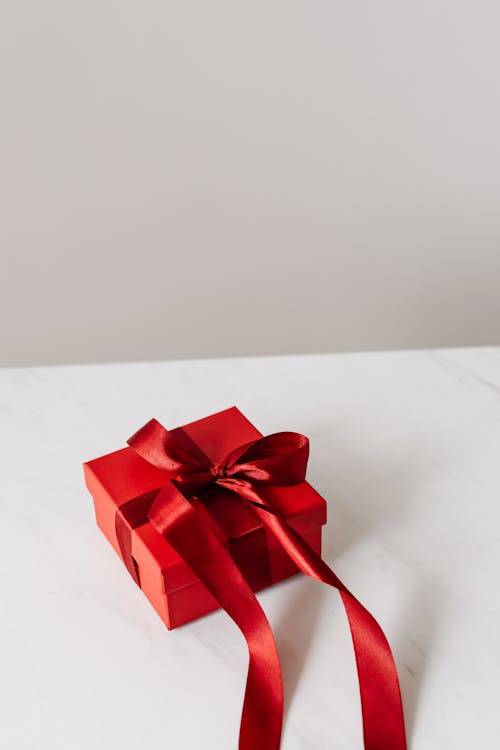 Free Red Gift Box With Red Ribbon on a White Surface Stock Photo